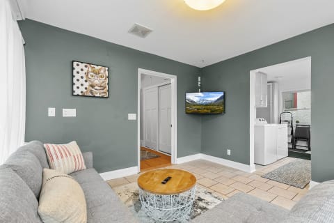 A stylish living room featuring a gray sofa, whimsical cat artwork, and a mounted TV.
