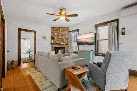 Cozy living room featuring a gray sectional sofa, stone fireplace, and a large television against a stylish accent wall.