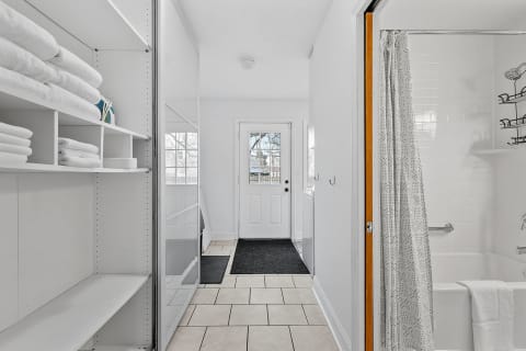 An airy entryway with open shelves of towels, a front door, and a shower curtain.