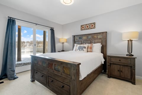 Cozy bedroom with wooden bed and lakeside view through large windows.