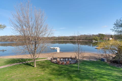 A peaceful lakeside scene featuring a tree, sandy beach, and clear blue skies.