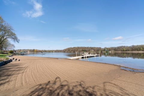 A scenic view of a sandy beach beside a calm lake with a dock.