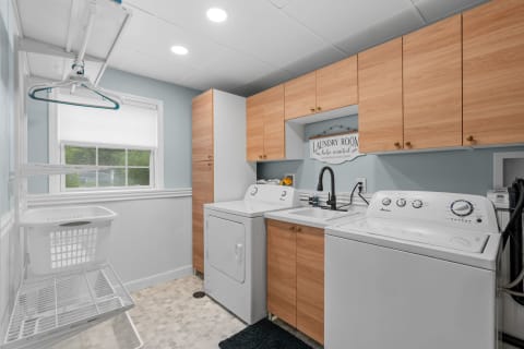 A spacious laundry room with a washing machine, dryer, sink, and wooden cabinetry.