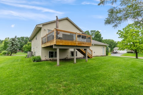 Two-story house with a wooden deck and green lawn under a clear blue sky.