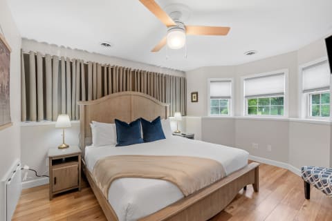 A beautifully decorated bedroom featuring a king-size bed with navy pillows, a stylish nightstand, and large windows with curtains.