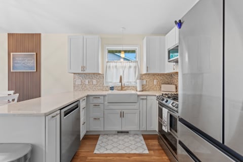 Modern kitchen featuring white cabinetry, a farmhouse sink, and warm wood flooring.