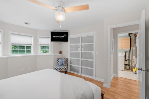 Cozy bedroom with light-colored walls, windows, a ceiling fan, and access to a laundry room.