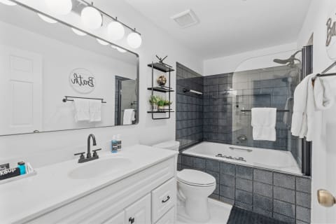 Modern bathroom with white vanity, black accents, and glass shower enclosure.