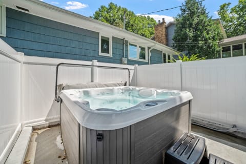 Hot tub in a backyard with a white fence and a blue house in the background.