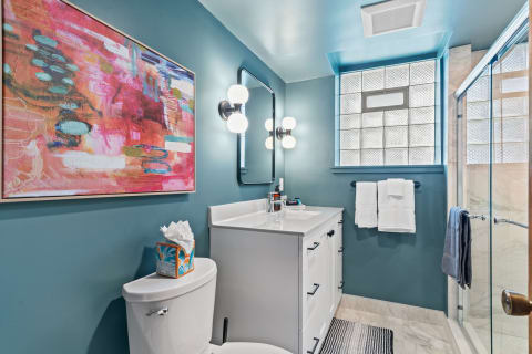 Interior view of a stylish bathroom featuring a colorful painting, a white vanity, and glass shower.