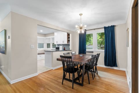 Dining room featuring a large wooden table, black chairs, a starburst chandelier, and adjoining kitchen area.