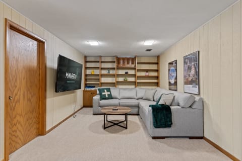 A cozy basement living room featuring a sectional sofa, a mounted TV, and decorative shelves.