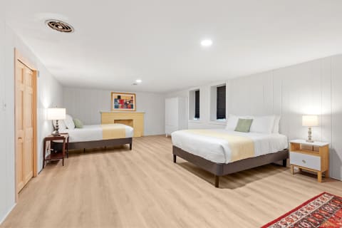 Spacious bedroom with two beds, light wooden flooring, and a yellow brick fireplace.