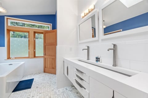 Modern bathroom with white vanity, blue walls, and mosaic tile floor.