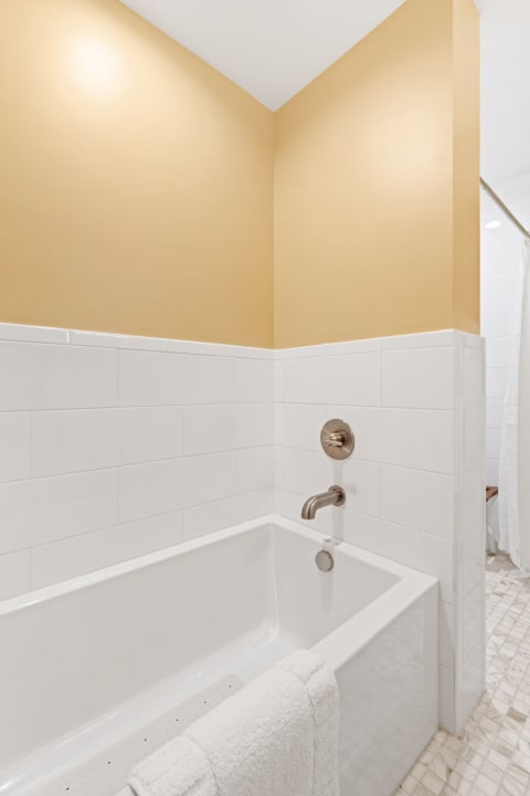 A bathroom with a white bathtub and yellow wall, showcasing a clean and modern design.