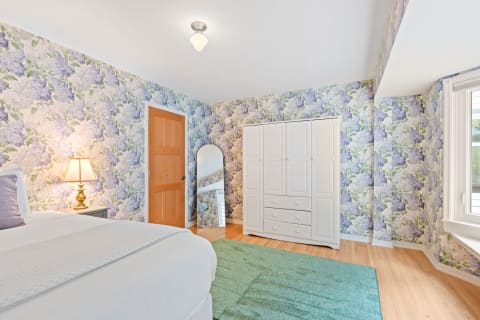 A floral-themed bedroom featuring a white bed, floral wallpaper, and a wardrobe.