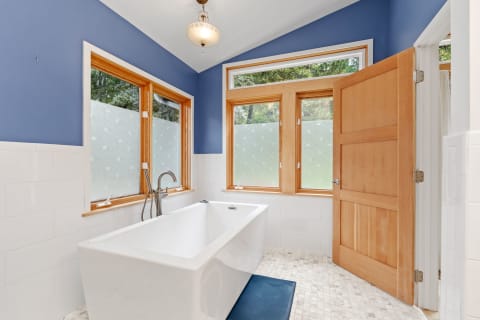 Modern bathroom with a freestanding bathtub, blue walls, and natural light.