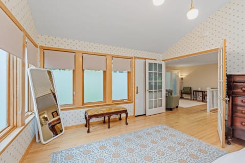 Bright room with patterned wallpaper, wooden floors, a vintage bench, and a full-length mirror.