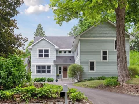 Light blue two-story house with white trim in a green landscape.