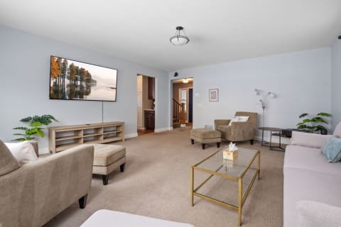 A living room with a gray couch, beige armchair, a glass coffee table, and a flat-screen TV showing a nature scene.