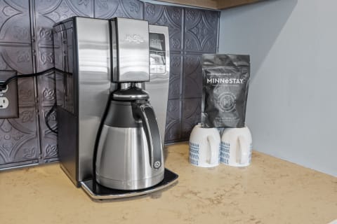 Modern coffee maker with a stainless steel carafe, a coffee bag, and two patterned mugs on a countertop.