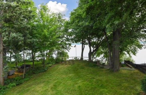 Lawn with green trees and chairs near a lake.