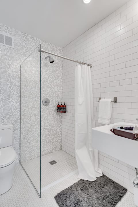 A modern bathroom with a glass shower, white sink, and grey bath mat.