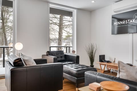 A modern living room featuring black leather sofas, large windows, and a wooden side table.