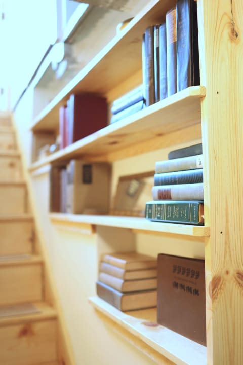 A wooden bookshelf with various books, illuminated by natural light, next to a staircase