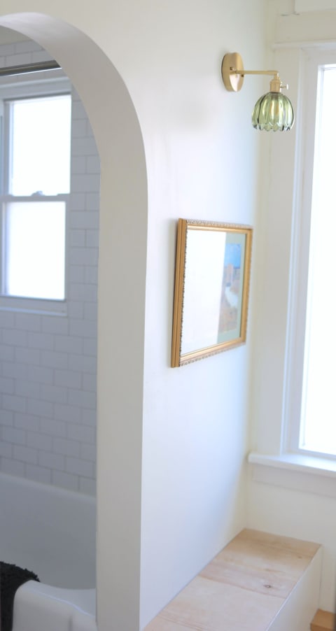 A bright bathroom with white walls, a gold-framed painting, and a green light fixture.