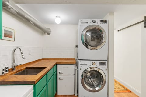 Modern laundry area with stacked washer and dryer, a stainless steel sink, and vibrant green cabinets.