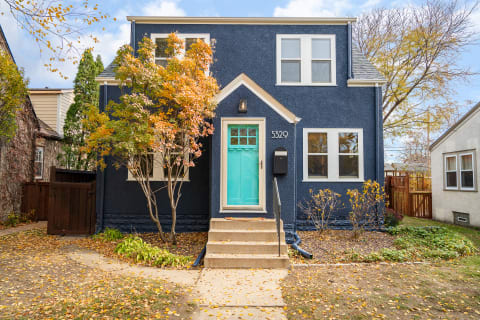 Two-story house with dark blue exterior and turquoise door, surrounded by autumn leaves.