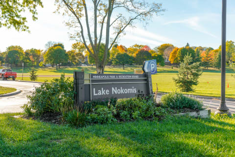 Lake Nokomis sign with lush greenery and autumn trees in the background.