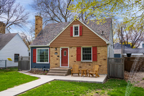 A cozy house featuring red shutters and a small patio with wooden chairs.