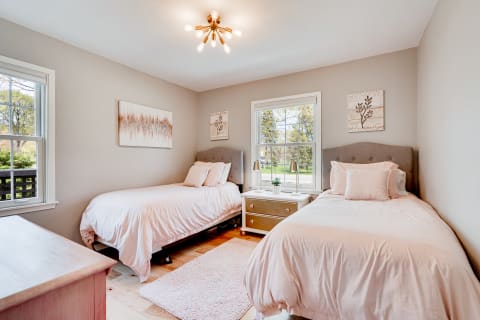 A twin bedroom featuring two beds, pastel decor, and natural light through a window.