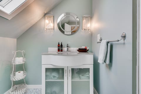 A small, stylish bathroom featuring pale blue walls, a white vanity, and elegant lighting.