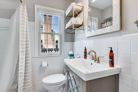 A view of a stylish bathroom featuring a white sink, modern fixtures, and neatly arranged towels on a shelf.