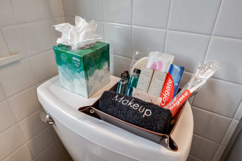 Bathroom essentials displayed on a toilet lid, including a towel, shampoo, toothpaste, and tissues.