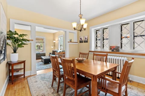 Bright dining room with wooden table, chairs, and a view into a living space.