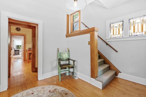 A bright entryway featuring stained glass windows, a wooden staircase, and a decorative chair.
