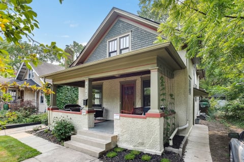 A two-story house with a porch, surrounded by green foliage.