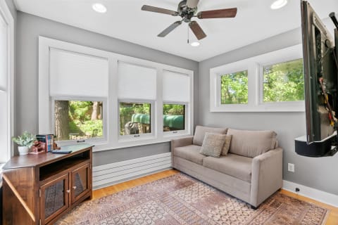A bright sunroom with a gray wall, a sofa, and a wooden table with plants and books.