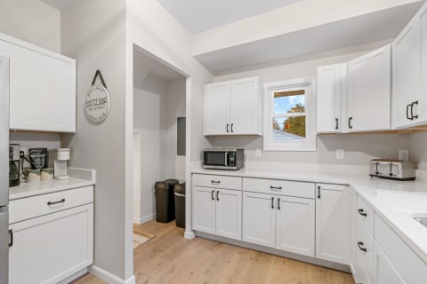 Modern kitchen with white cabinets, coffee bar, and natural light from a window.