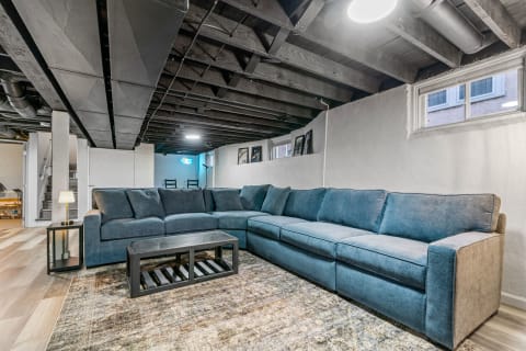 A large blue sectional sofa in a cozy basement living area with a coffee table and framed artworks.