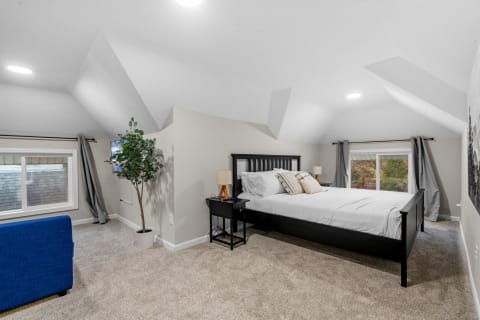 A modern attic bedroom featuring a black bed, indoor plants, and a blue couch.