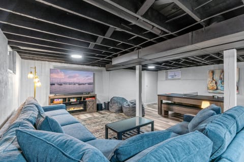 A cozy basement featuring a blue sectional sofa, large TV, and ping pong table.