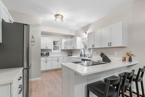 Modern kitchen featuring white cabinets, quartz countertops, and black chairs around an island.