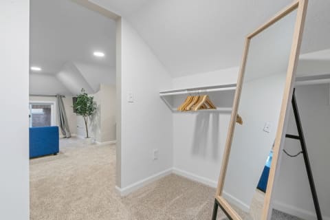 A minimalistic closet area featuring a full-length mirror, wooden hangers, and a glimpse of a living room with a blue sofa.