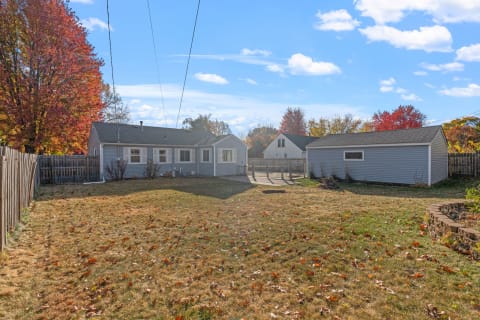 Backyard view of a blue house with autumn leaves and a storage shed.