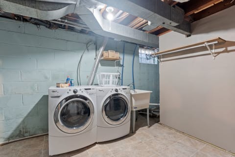 Laundry area in a basement featuring front-loading washers, a laundry sink, and a small shelf.